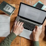 Copywriting for Small Businesses: Small business owner writing marketing copy on a laptop with a notebook and coffee on the desk